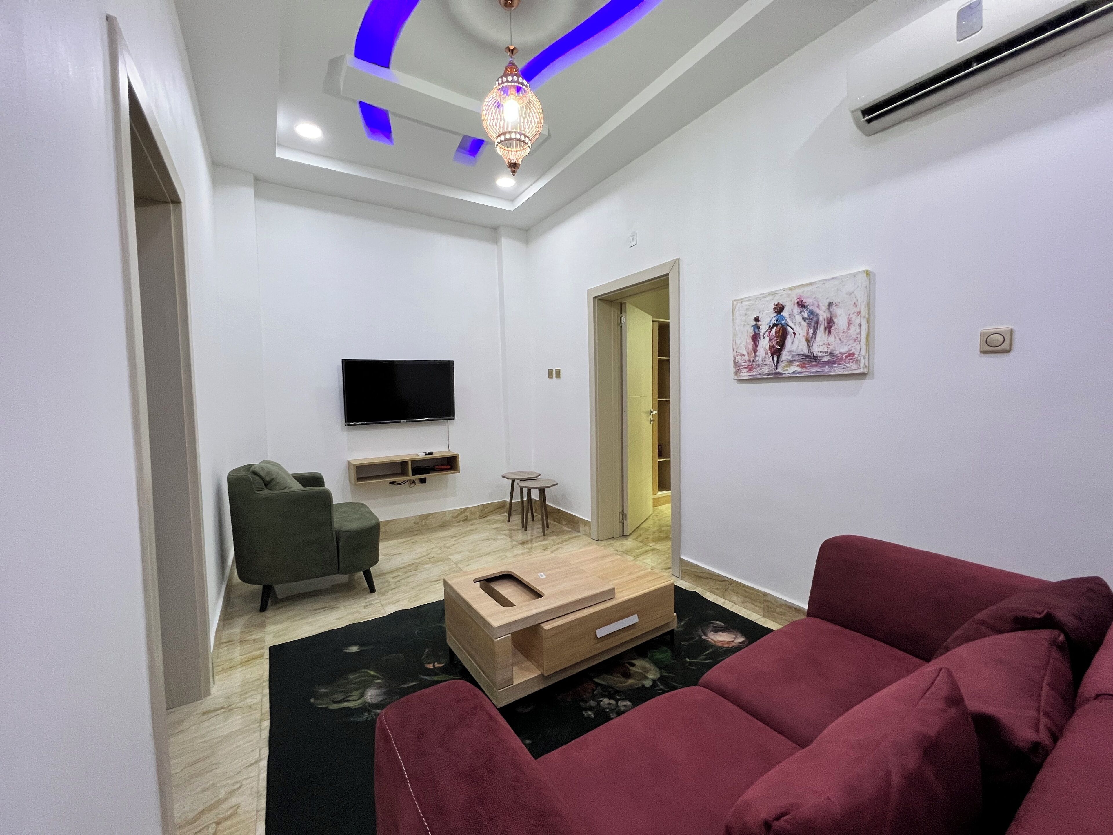Uma sala de estar moderna com uma TV de tela plana, uma poltrona verde, um sofá vermelho, uma mesa de centro de madeira e um lustre decorativo.