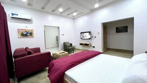 Una habitación de hotel con cama, un sofá rojo, televisión y aire acondicionado.