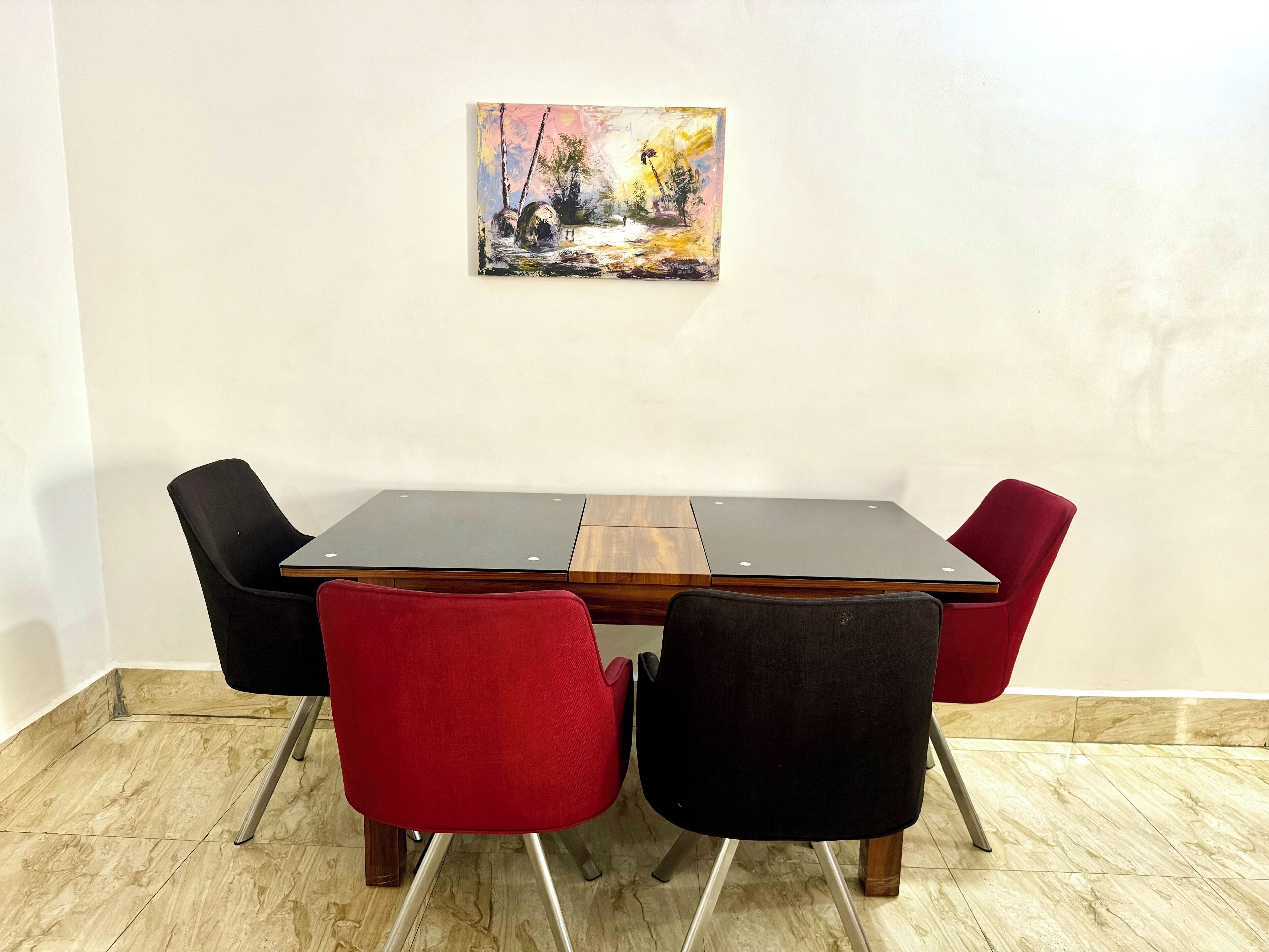 A dining table with four chairs, a painting on the wall, and a tiled floor.