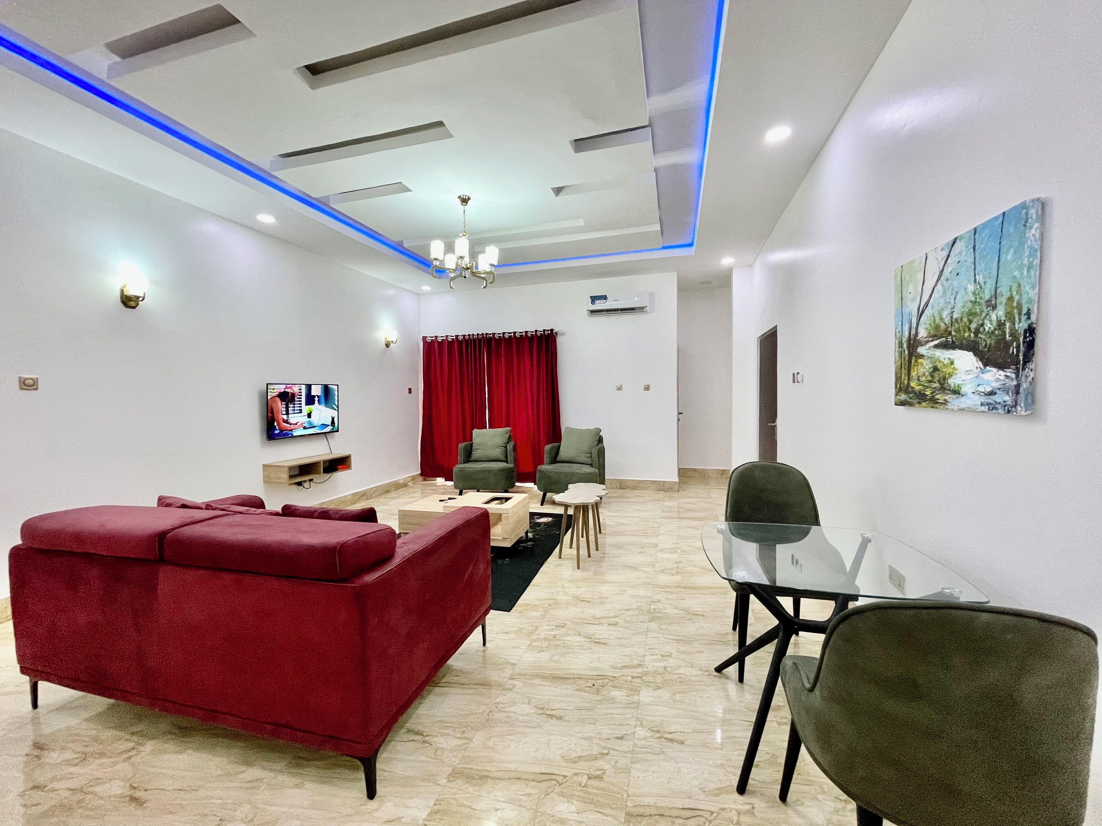 A modern living room with a red sofa, a glass table, and a TV on the wall.
