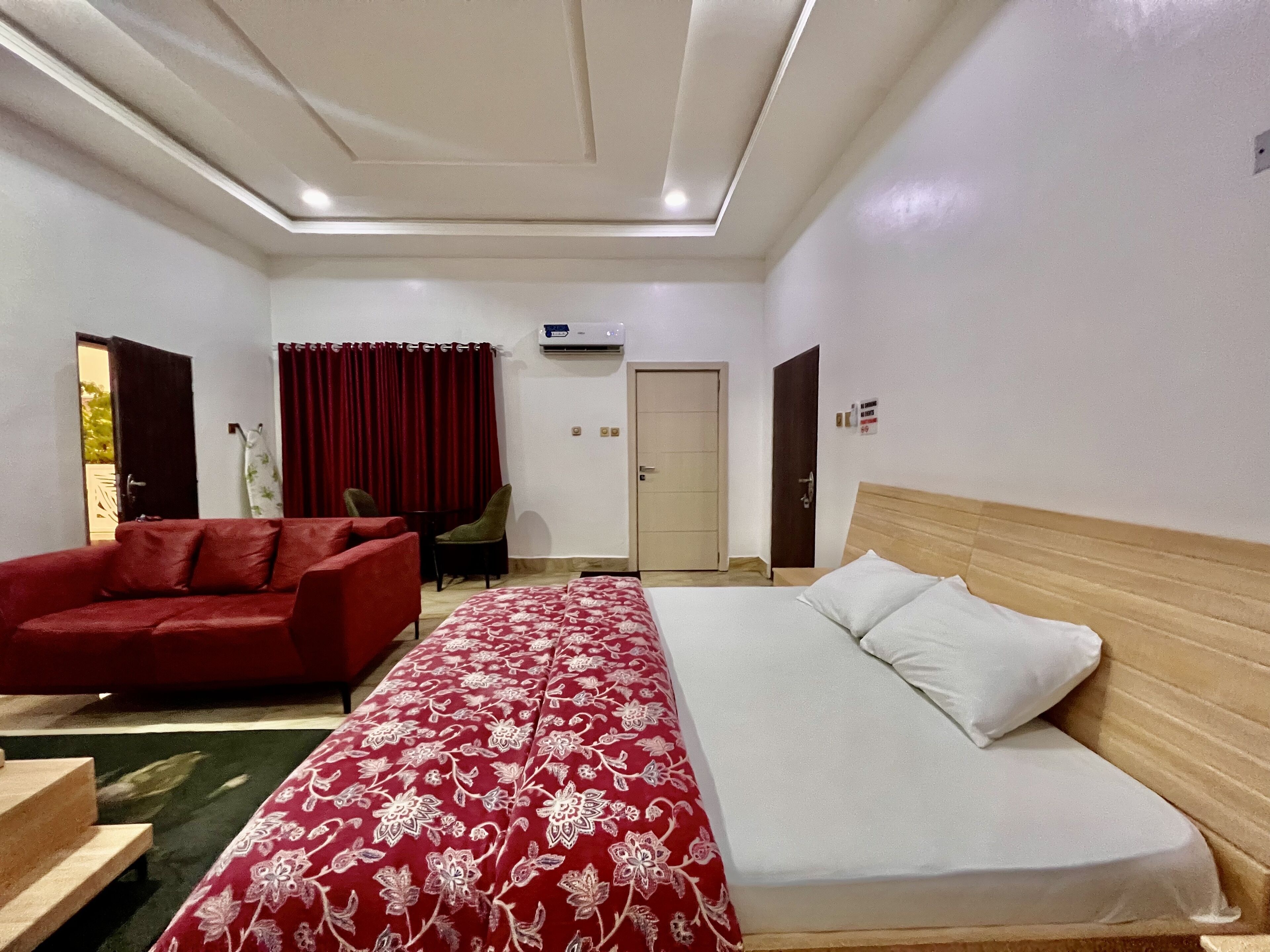A hotel room with a bed, a red sofa, a small table, and a chair.