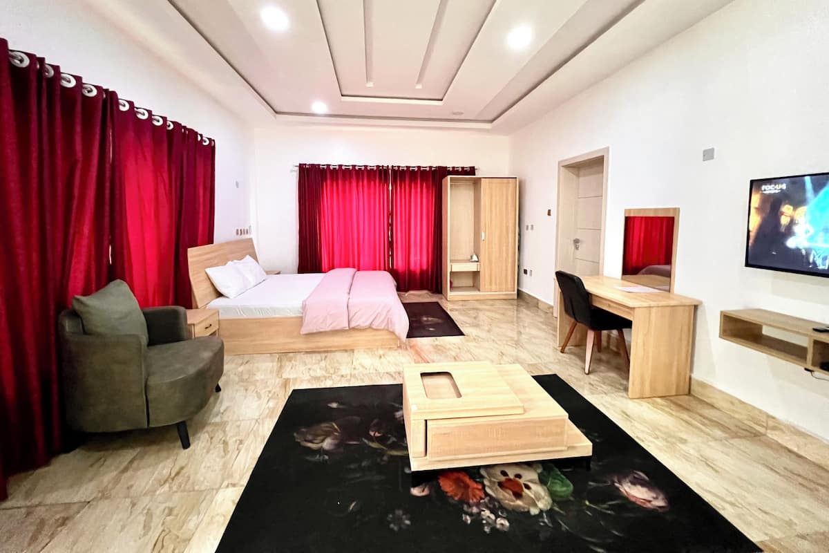 Une chambre d’hôtel moderne équipée d’un lit, d’un bureau, d’une chaise, d’une télévision et de rideaux rouges.