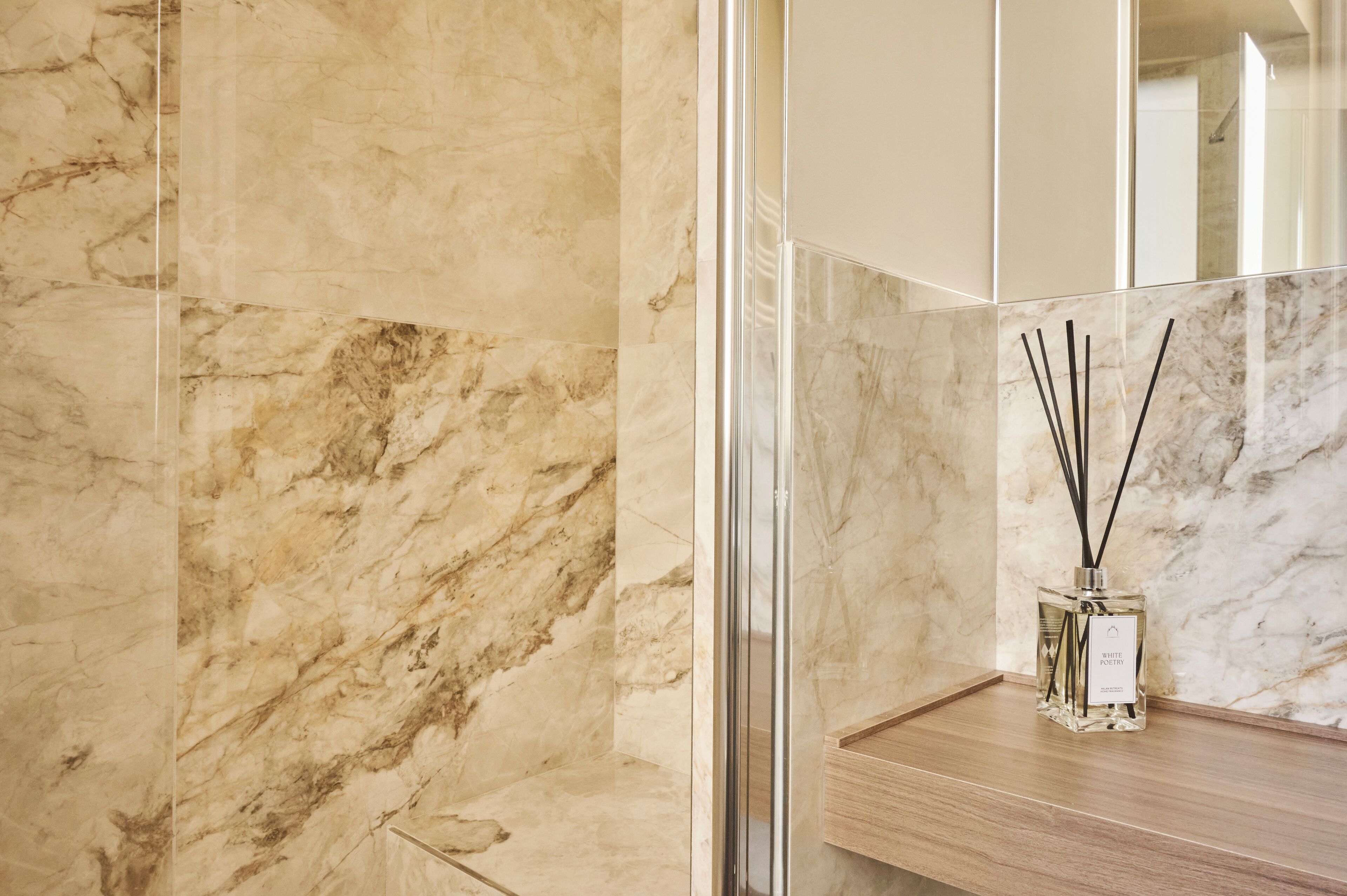 A bathroom with marble walls, a wooden vanity, and a glass shower enclosure.