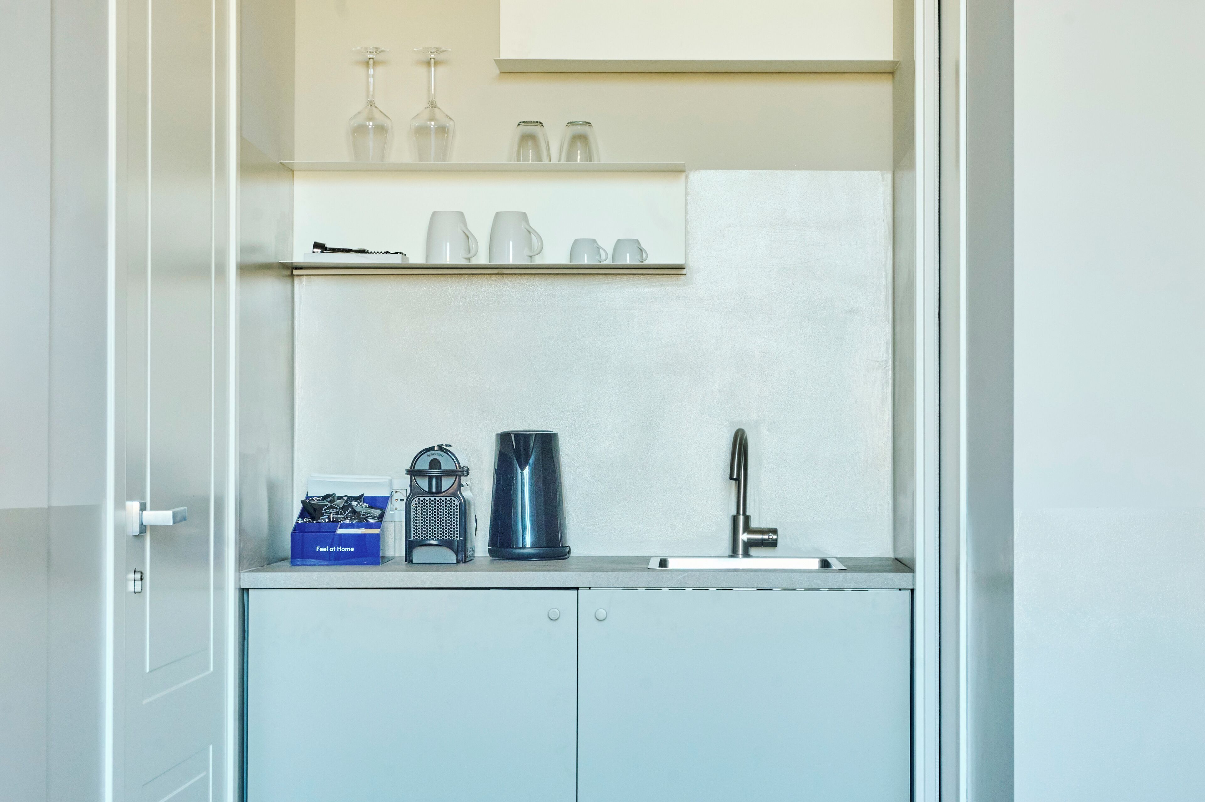 A compact kitchen with a sink, a coffee maker, and a kettle on the counter.