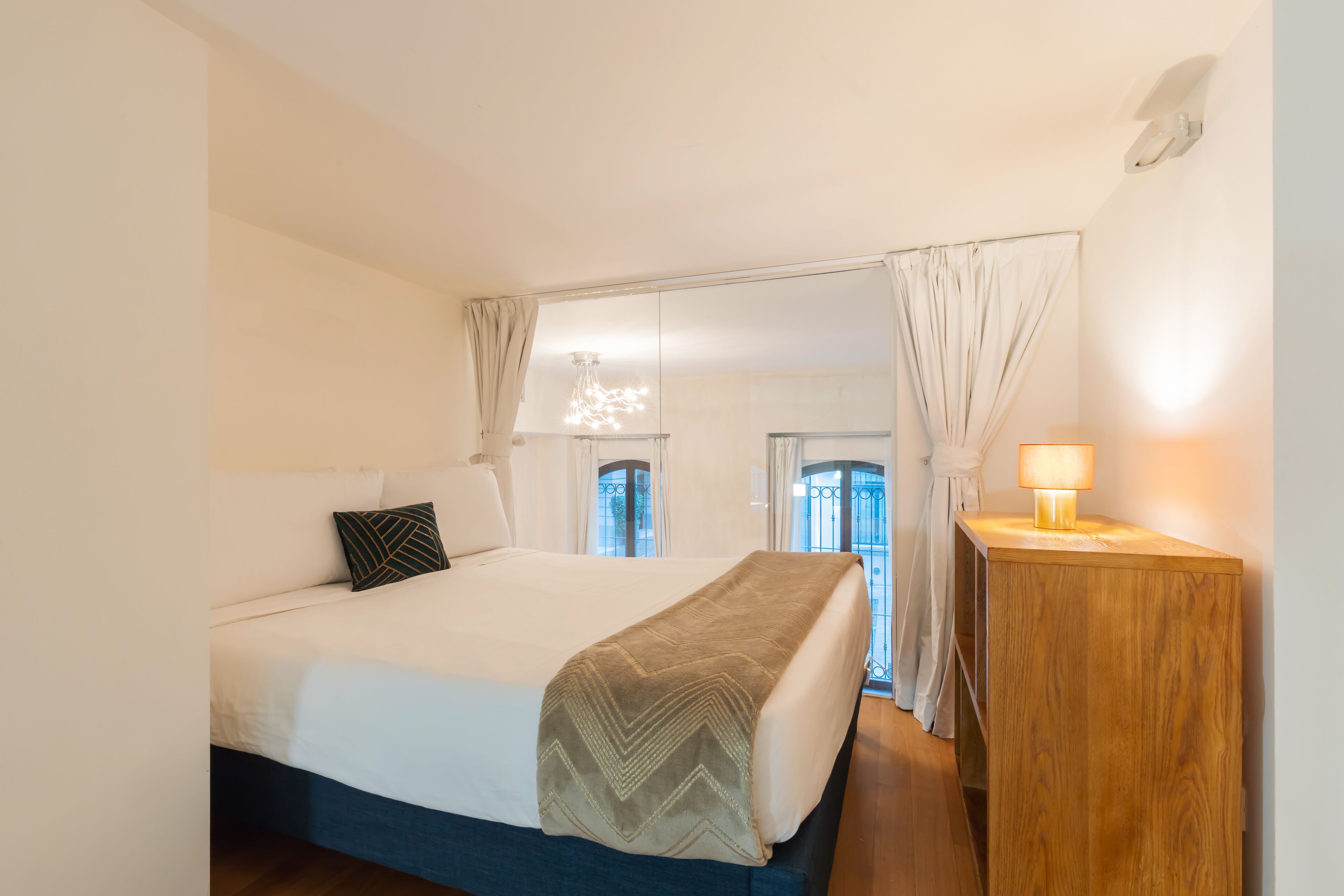 Een slaapkamer met een bed, nachtkastje en uitzicht door een raam.