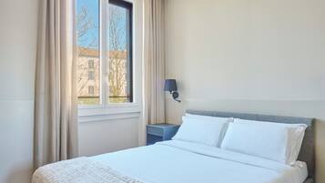 A hotel room with a bed, a nightstand, a lamp, and a window with curtains.