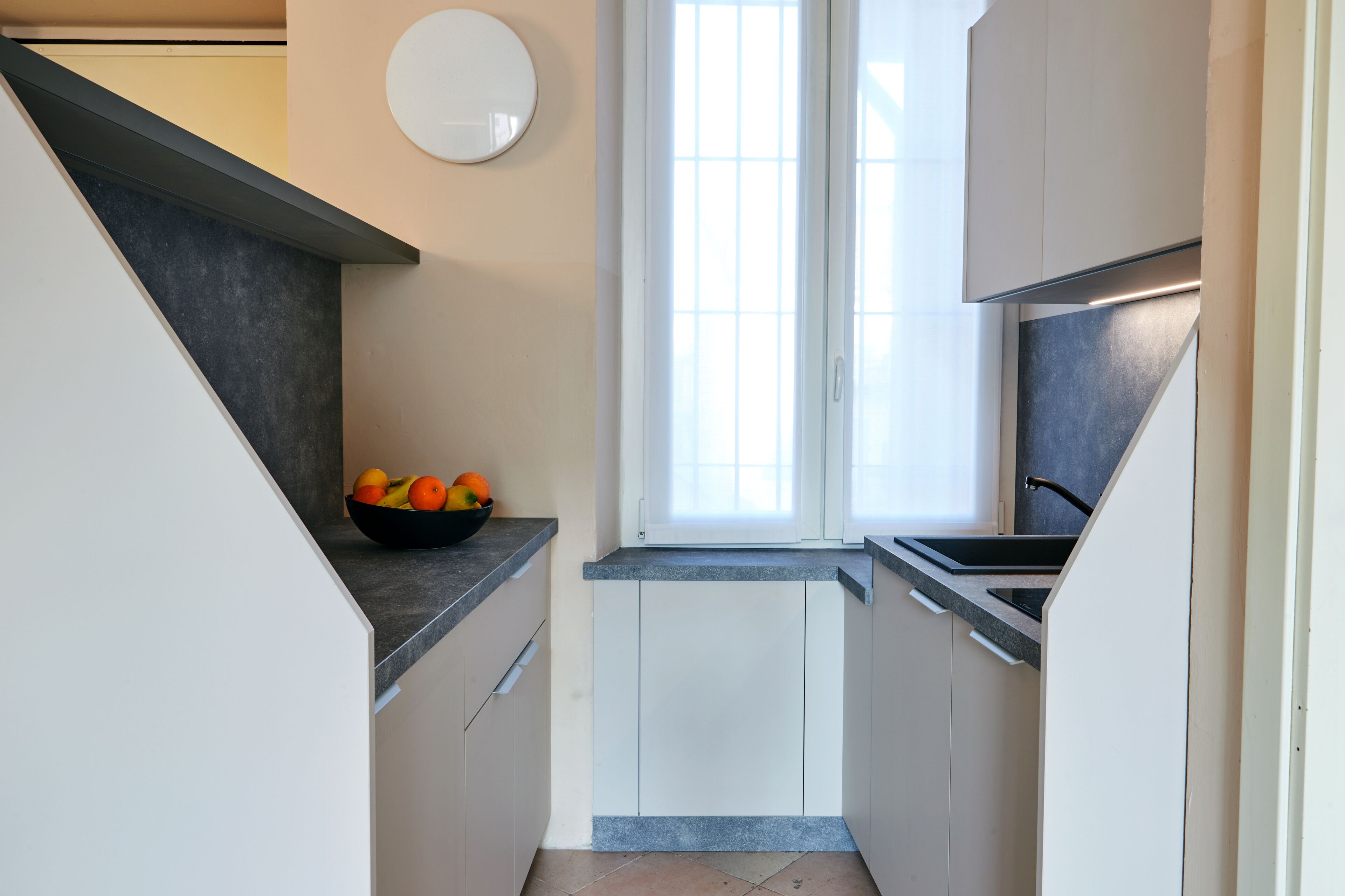 A modern kitchen with a black countertop, white cabinets, and a bowl of fruit on the counter.