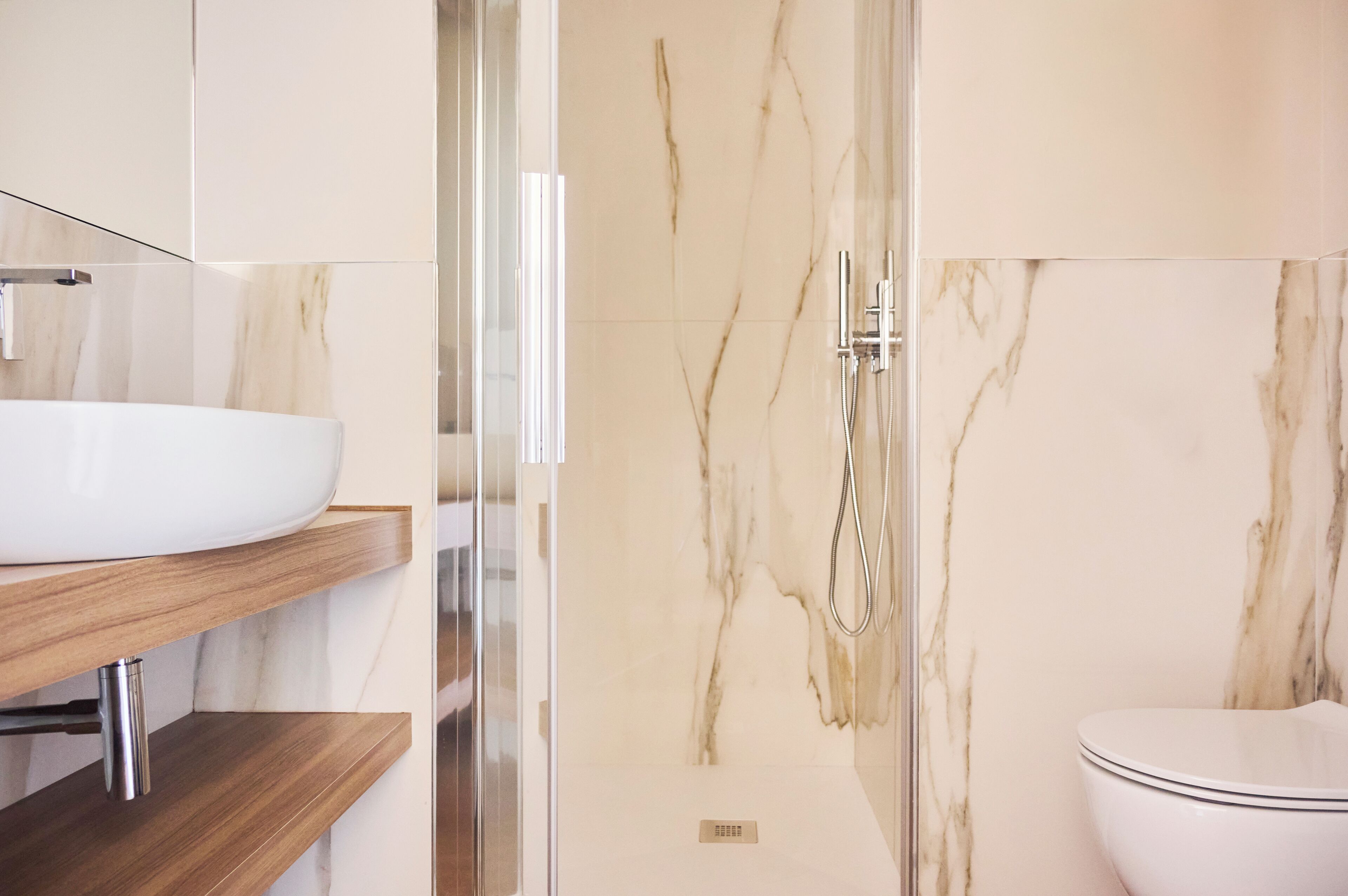 A bathroom with a white sink, wooden shelves, a glass shower enclosure, and a toilet.