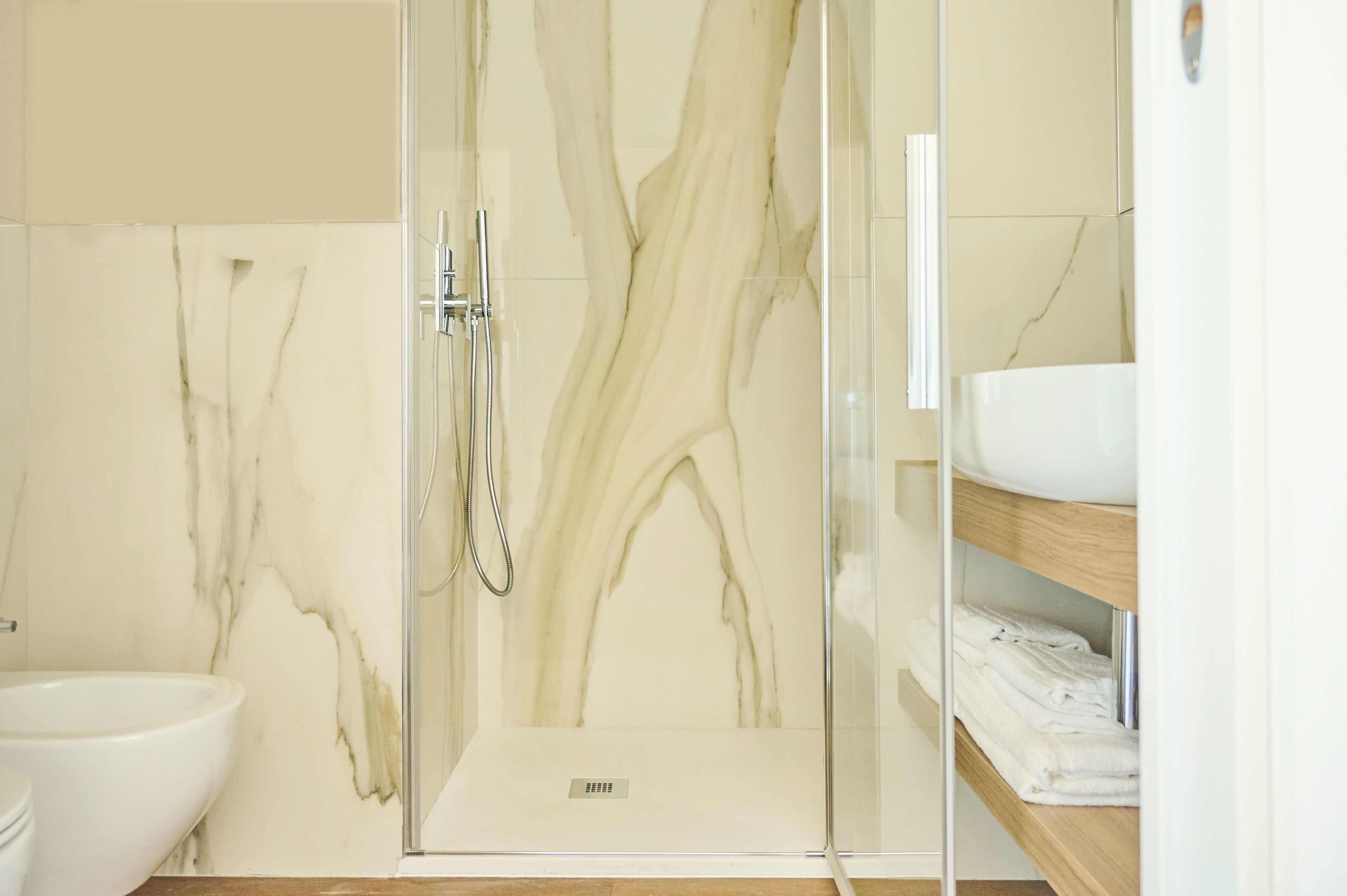 Un baño moderno con ducha de vidrio, lavamanos blanco y paredes de mármol.
