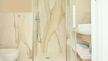 Un baño moderno con ducha de vidrio, lavamanos blanco y paredes de mármol.