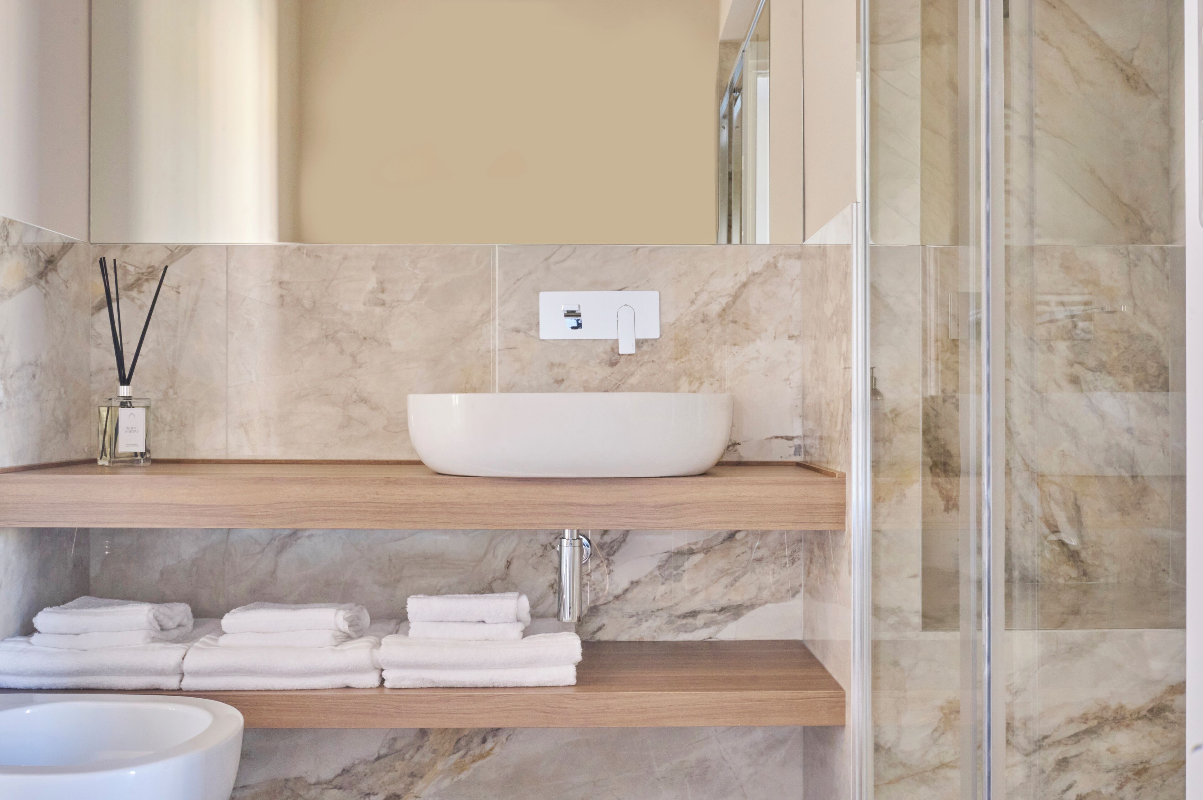 Une salle de bain avec un lavabo en marbre, des étagères en bois et une cabine de douche en verre.