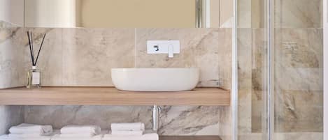 Une salle de bain avec un lavabo en marbre, des étagères en bois et une cabine de douche en verre.