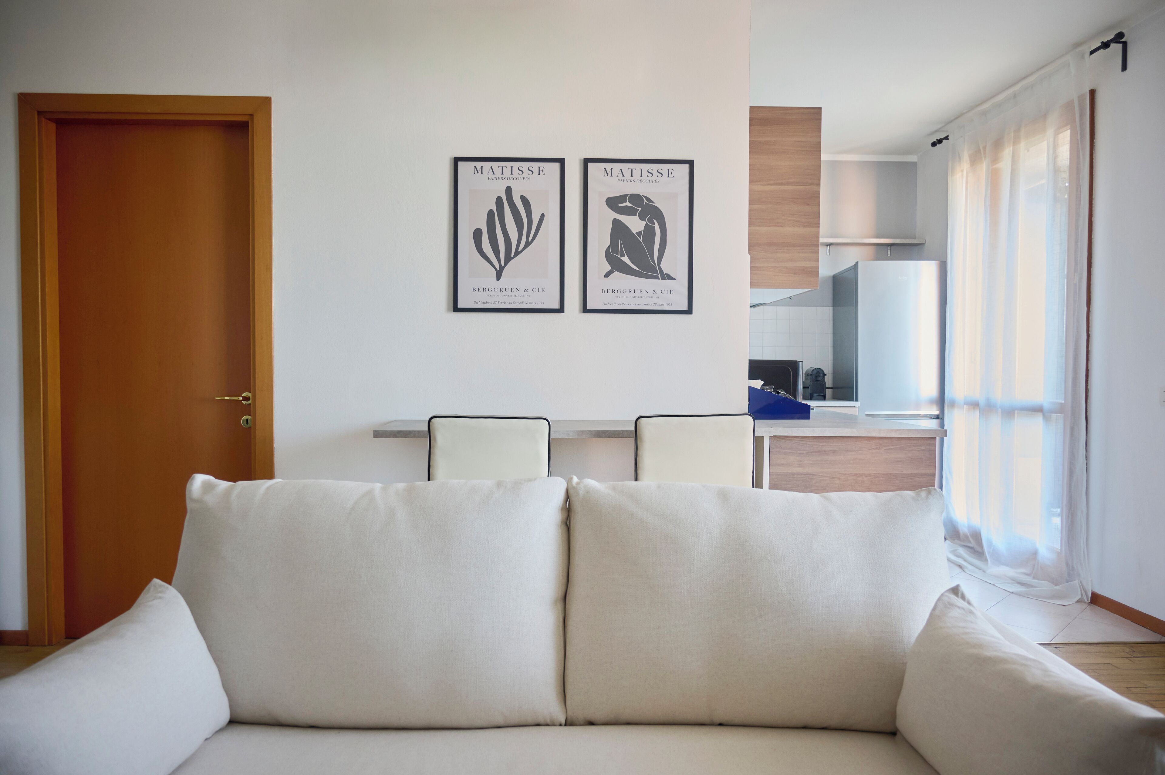 Un salon avec un canapé, une porte en bois, un coin cuisine et deux œuvres d’art encadrées accrochées au mur.