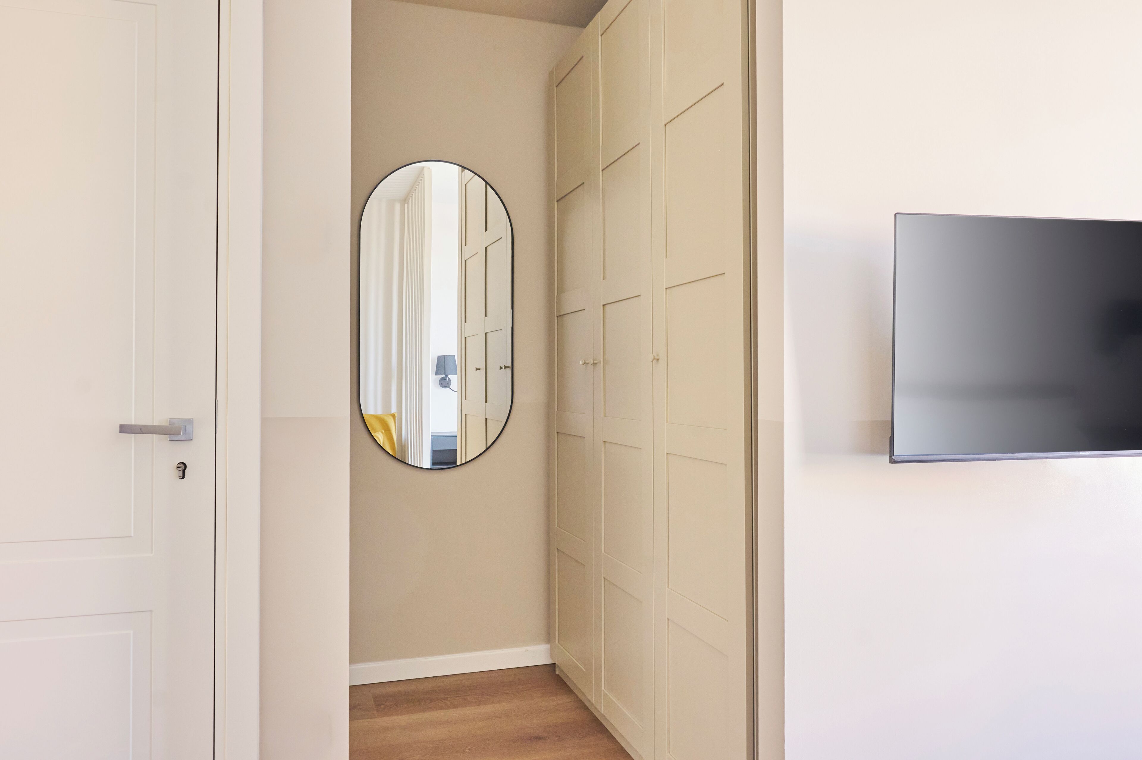 A hallway with a door, a mirror, a wardrobe, and a TV on the wall.