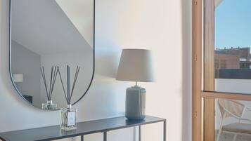 A modern room with a large mirror, a table with a lamp and perfume bottles, and a view of the outside.