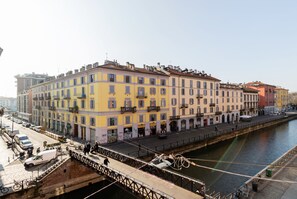 A multi-story building with balconies, a river in the foreground, and a bridge with a pedestrian walkway. - Milan Retreats Navigli (Milan)