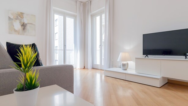 A modern living room with a flat-screen TV, a sofa, a coffee table, and a potted plant. - Milan Retreats Navigli (Milan)