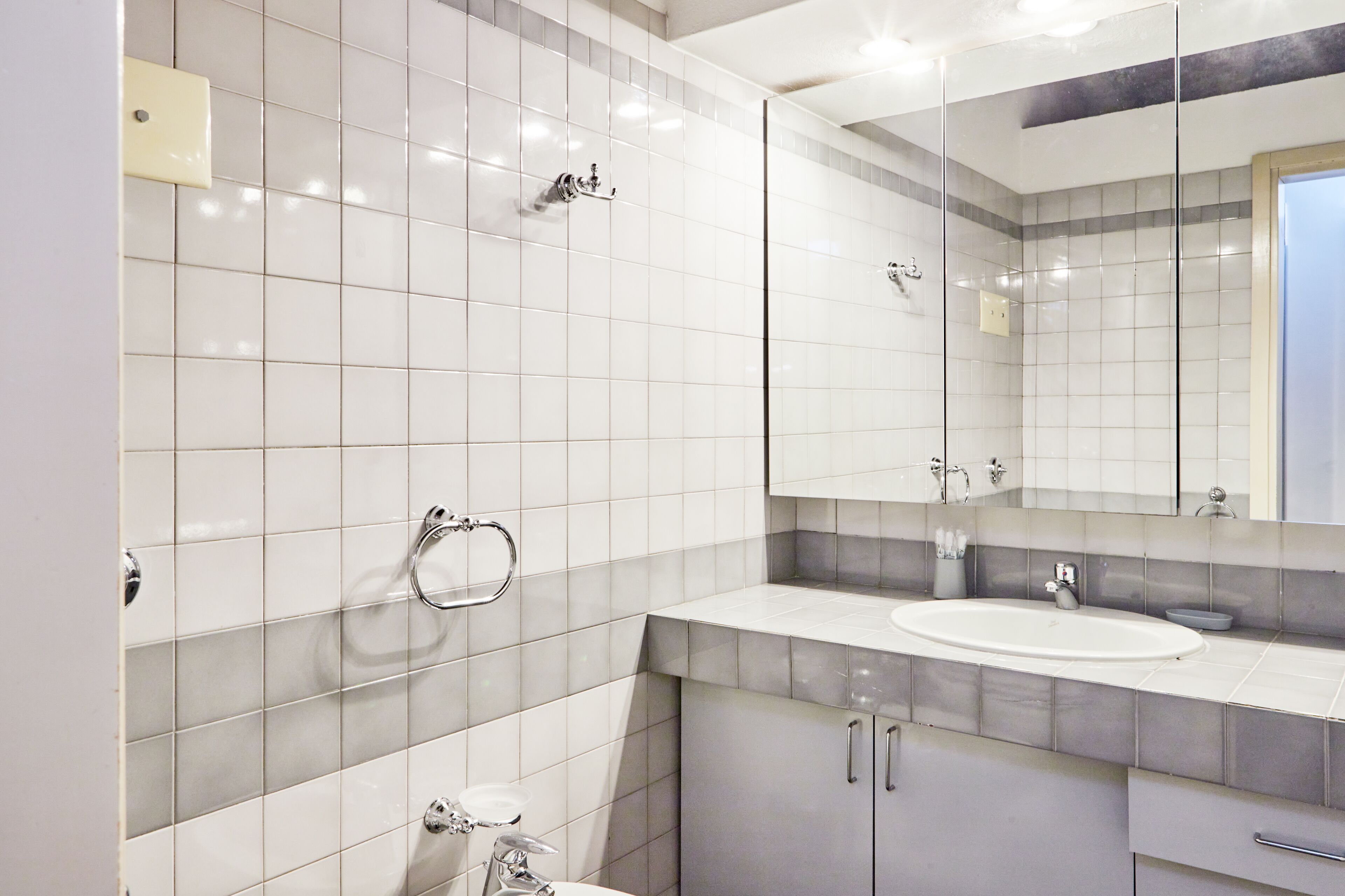 Ein modernes Badezimmer mit weißen Fliesen, einem großen Spiegel, einem Waschbecken und einer Toilette.