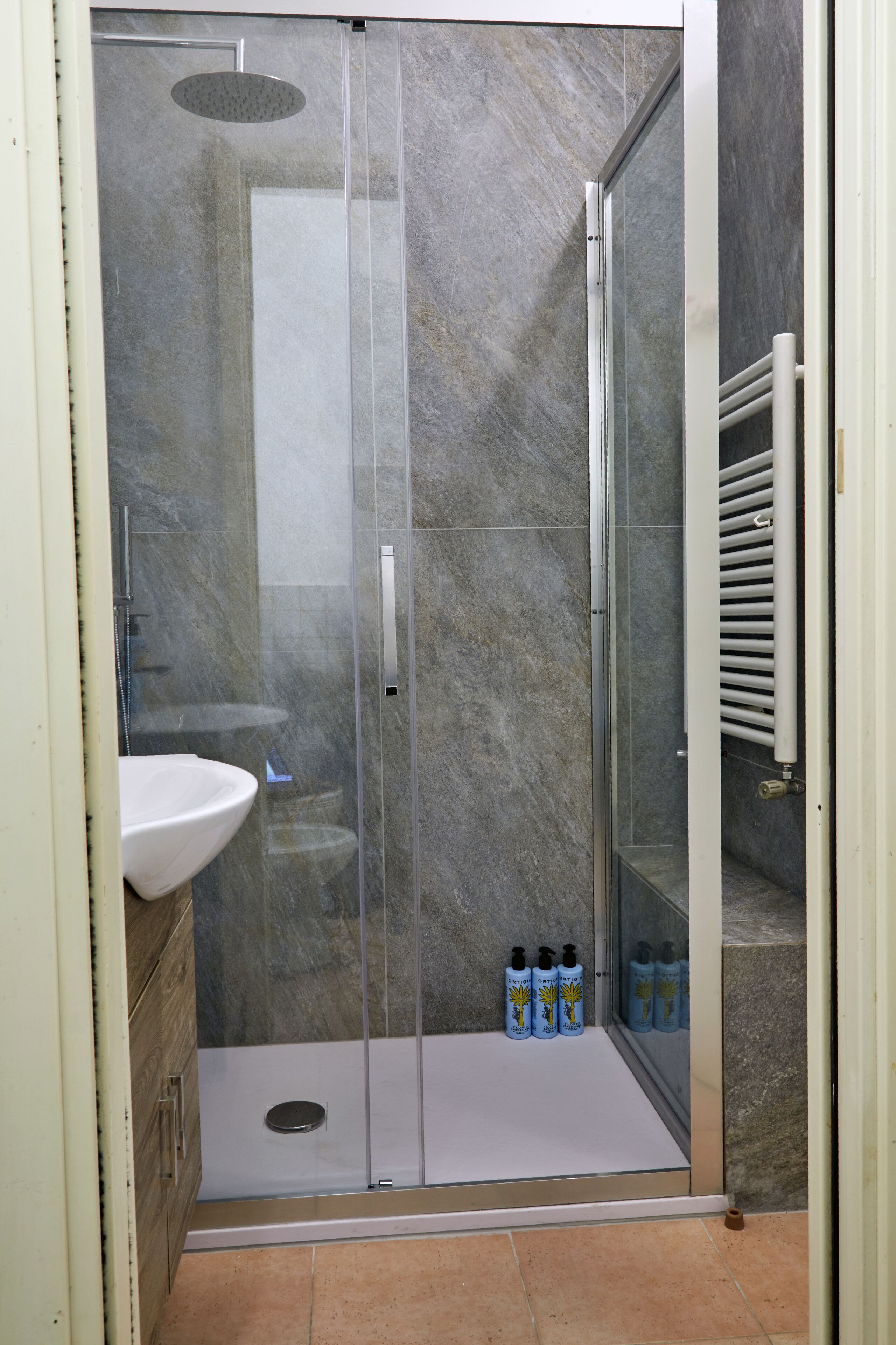 A bathroom with a glass-enclosed shower, a white sink, and a tiled floor.