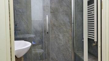 A bathroom with a glass-enclosed shower, a white sink, and a tiled floor.