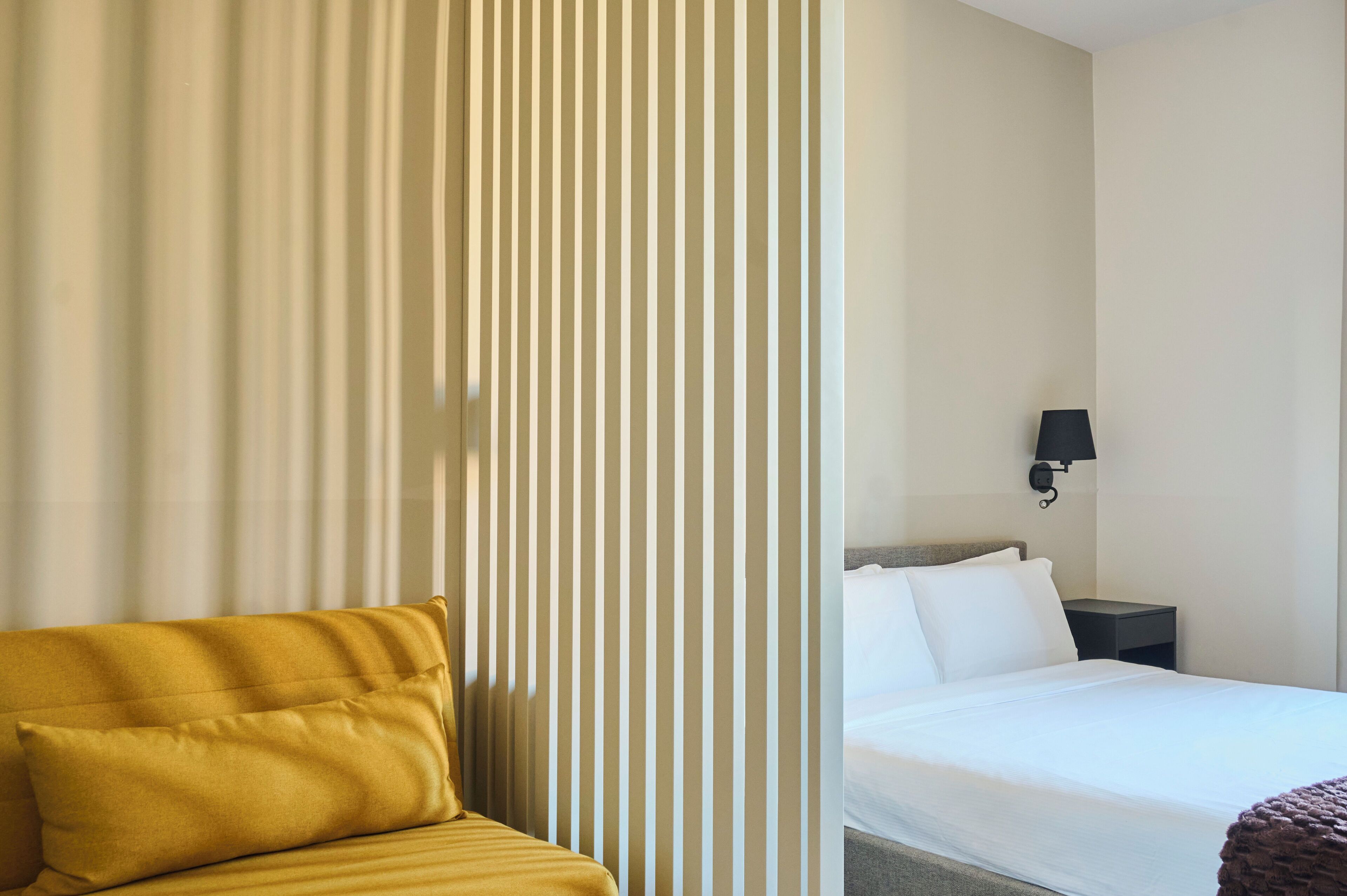 Una camera d'albergo con un letto, un comodino, una lampada e un divano.