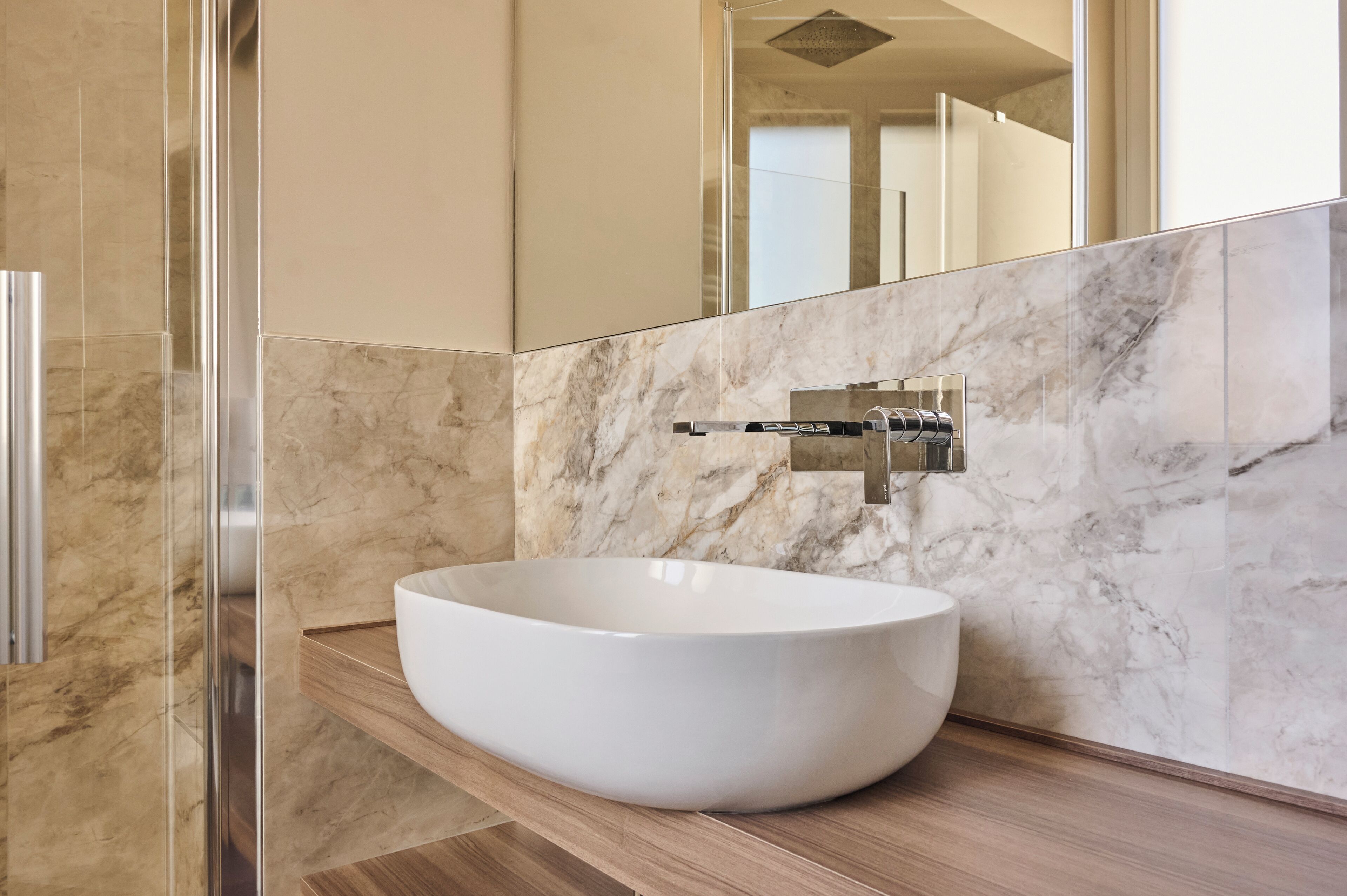 A modern bathroom with a large white vessel sink, a mirror, and a shower.