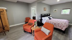 A bedroom with two orange armchairs, a bed with a floral bedspread, a nightstand, and a wooden wardrobe.