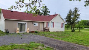 A single-story house with a red roof and beige siding, a front porch with a bench, and two lion statues on the front steps.