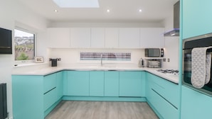 A modern kitchen with teal cabinetry, a skylight, and a view of the outdoors. - Ingledene (Brixham)