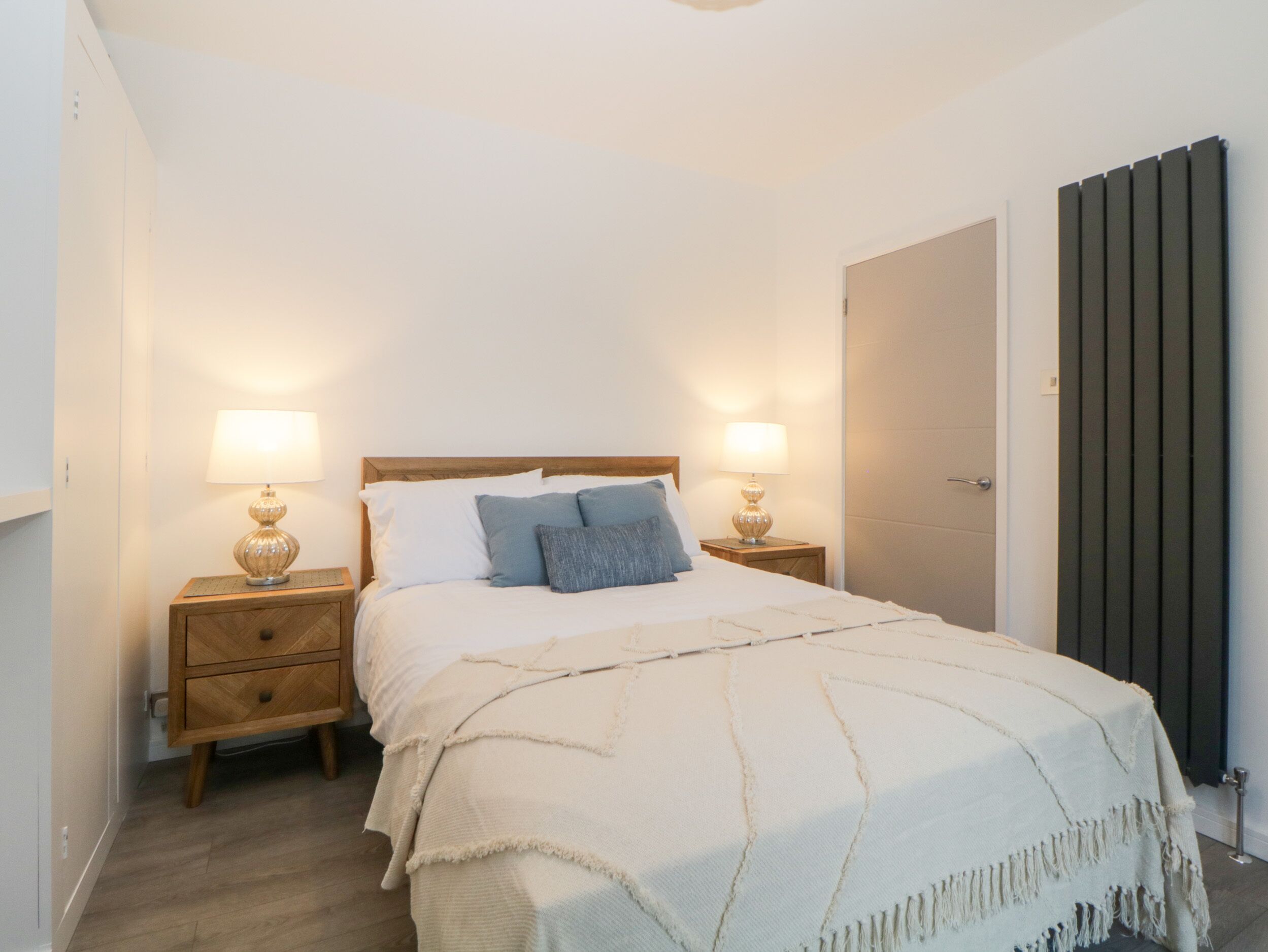 Una camera da letto con un letto di legno, due comodini con lampade, un tavolino di legno e una porta con termosifone.