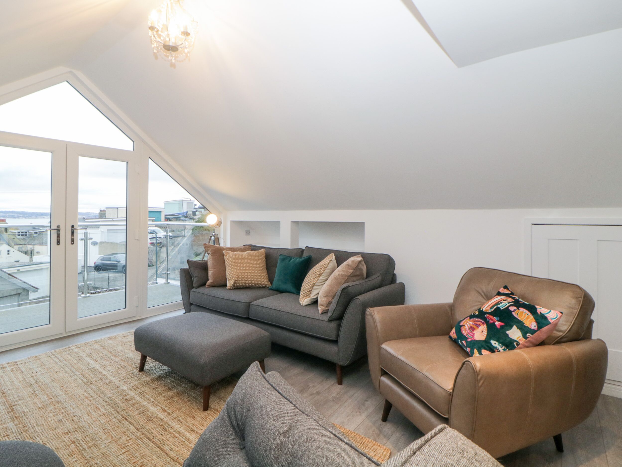 A modern loft apartment with a grey sofa, a brown armchair, and a large window offering a city view.