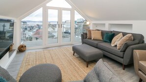 A modern loft apartment with a large skylight, a grey sofa set, and a view of the cityscape. - Ingledene (Brixham)