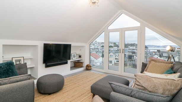 A modern living room with a large TV, comfortable seating, and a view of the city through large windows.