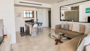 A modern living room with a sofa, a coffee table, a TV, and a kitchen area with a dining table and chairs. - Maon Saphir in Tel Aviv-yafo (Tel Aviv)