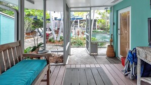 Un porche cubierto con un banco de madera, vista a una piscina y un área de estar al aire libre.