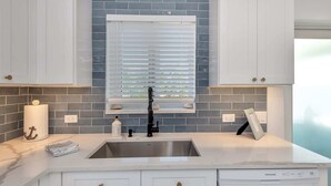 Una cocina con armarios blancos, un lavamanos de acero inoxidable y una ventana con persianas.
