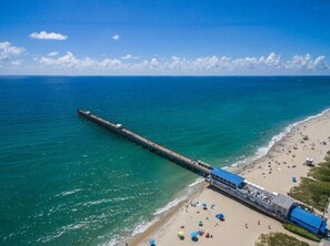 Un muelle que se adentra en el océano, con una playa y sombrillas de playa en la orilla.