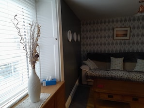 A living room with a sofa, a coffee table, a vase with dried plants, and a window with blinds. - Charming Eyemouth 1-bed Apt, Sleeps 2 Near Beach (Eyemouth)