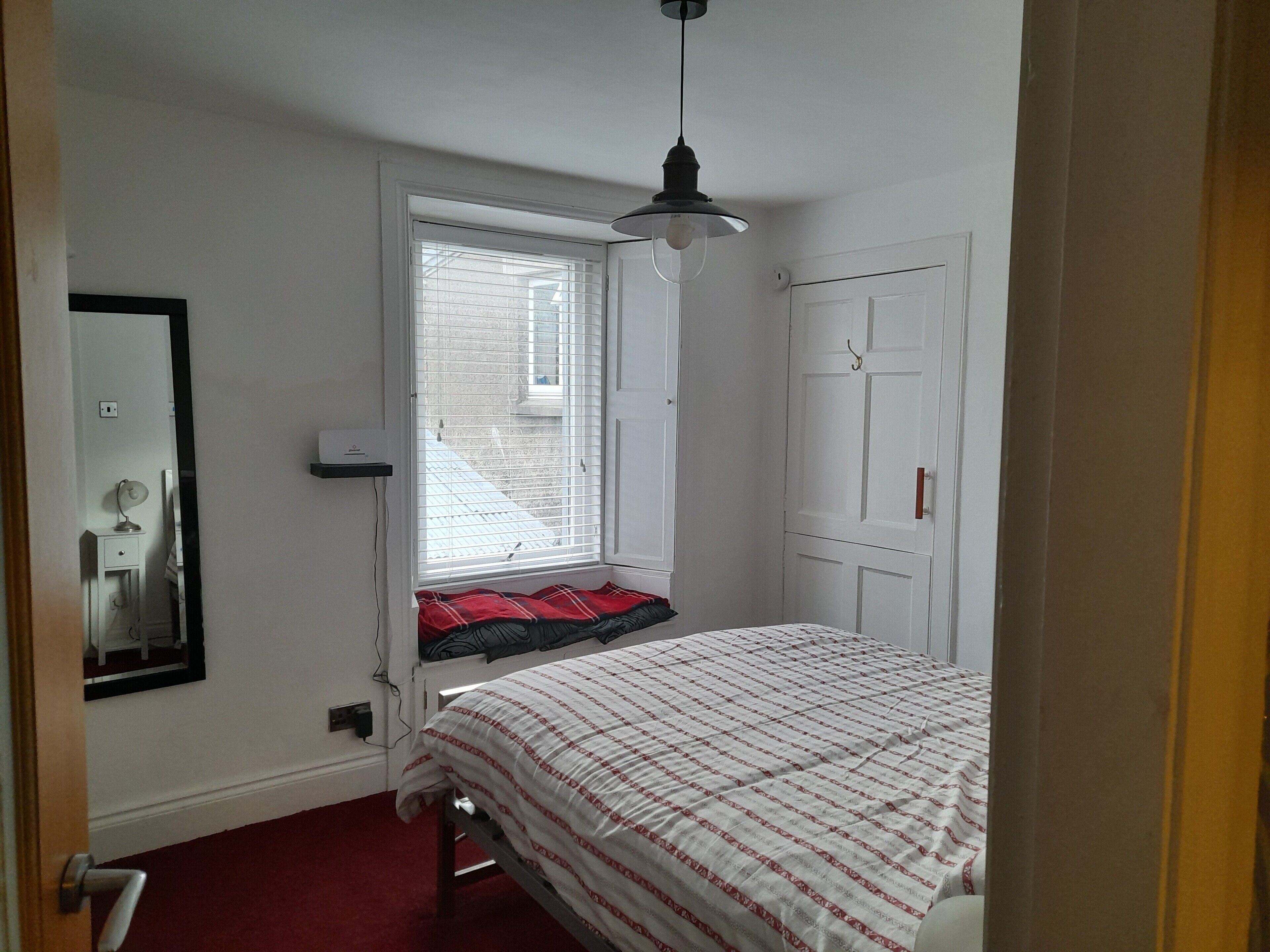 A bedroom with a bed, a window with blinds, a door, and a hanging light fixture.