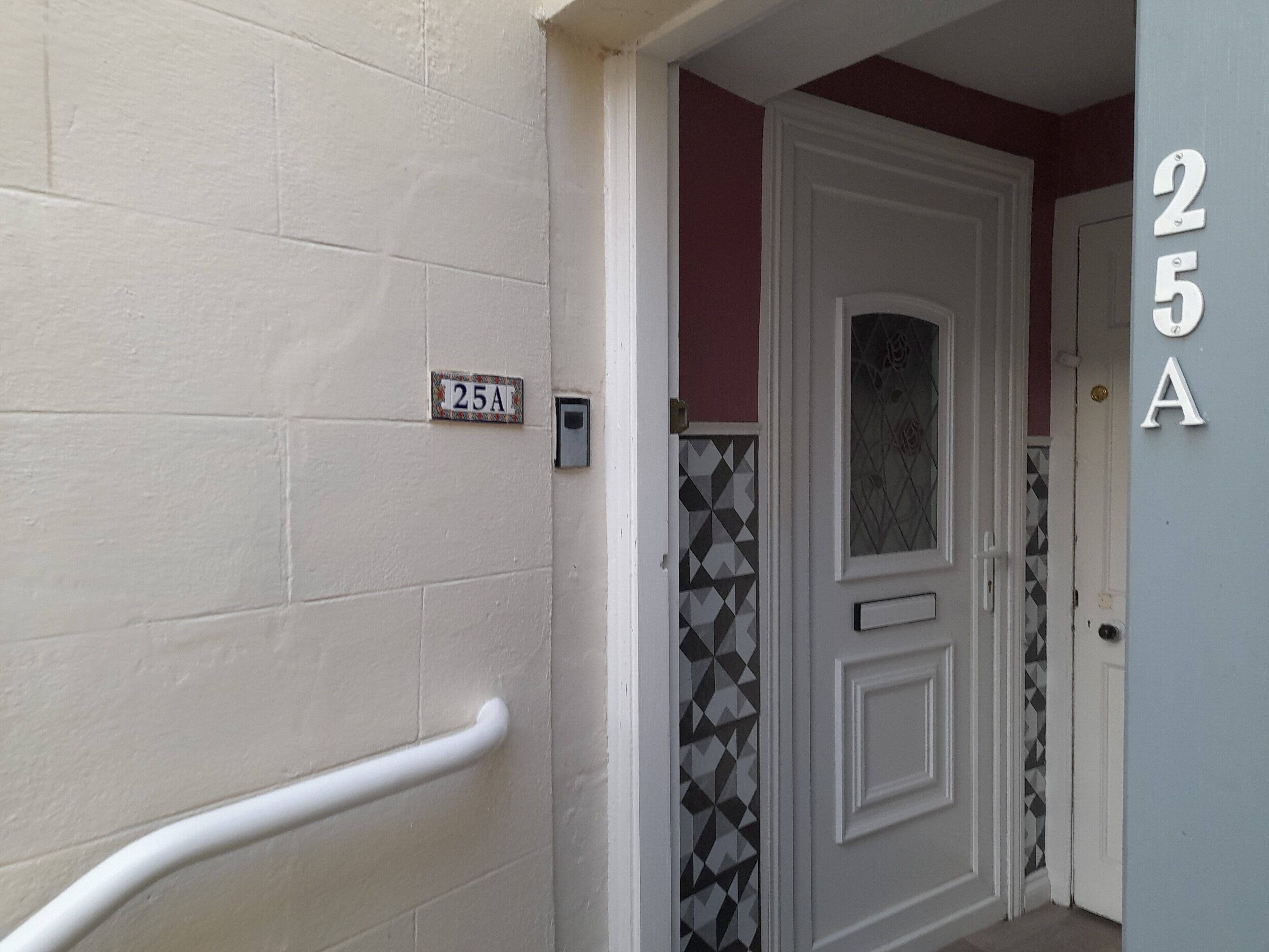 Un couloir avec une porte blanche, une boîte aux lettres et une plaque portant le numéro « 25A ».