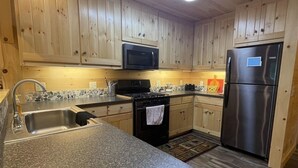 Una cocina con armarios de madera, encimera de granito, refrigerador de acero inoxidable y microondas.