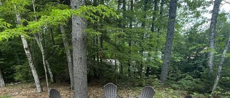A circular outdoor seating area with Adirondack chairs and a central table, surrounded by a gravel path and bordered by rocks.