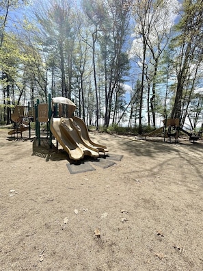 Un parque infantil con un tobogán y columpios, rodeado de árboles.