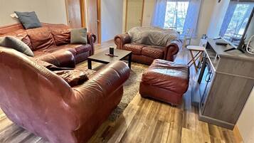 A spacious living room with leather sofas, a wooden floor, and a ceiling fan.