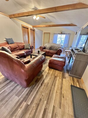 A spacious living room with leather sofas, a wooden floor, and a ceiling fan. - Crooked River Cottage Limit 5 2 Bedroom Cottage by RedAwning (Casco)