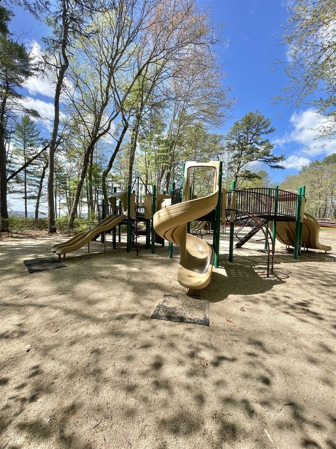 A playground with a spiral slide and a climbing structure, surrounded by trees and a clear sky.