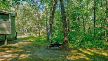 A rustic cabin with a small fire pit in a forested area.