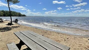 A wooden bench on a sandy beach with a clear sky and calm sea in the background.