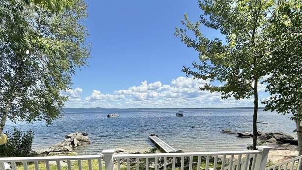 En terrass med två vita stolar och ett litet bord, med utsikt över en vattenyta med båtar och en brygga.