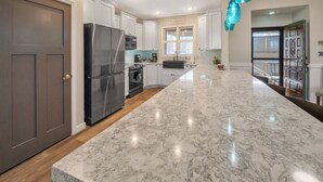 Una cocina moderna con armarios blancos, un refrigerador negro, una lámpara colgante color turquesa y una encimera de mármol.